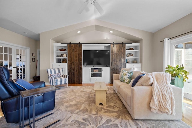 living room featuring french doors, lofted ceiling, light wood-type flooring, ceiling fan, and a barn door