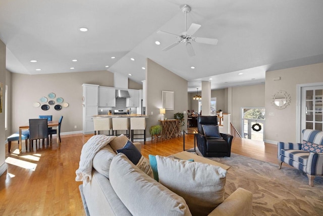 living room with high vaulted ceiling, ceiling fan with notable chandelier, and light hardwood / wood-style floors