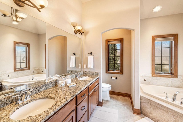 bathroom featuring tile patterned flooring, vanity, a relaxing tiled tub, and toilet