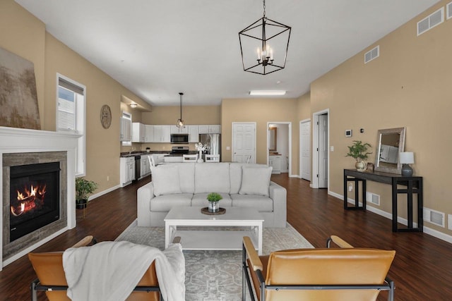 living room with dark wood-type flooring, a tiled fireplace, and a notable chandelier