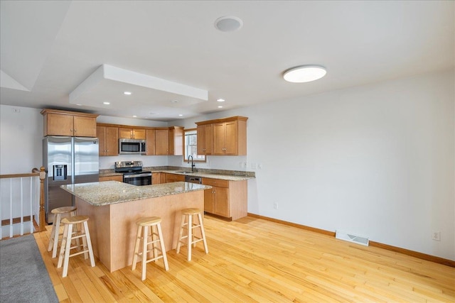 kitchen featuring a kitchen island, appliances with stainless steel finishes, sink, a breakfast bar area, and light hardwood / wood-style flooring