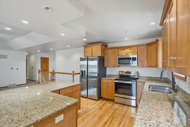 kitchen with appliances with stainless steel finishes, sink, light stone counters, and light wood-type flooring