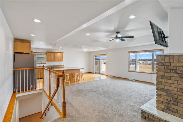 unfurnished living room with sink, light carpet, ceiling fan, and a tray ceiling