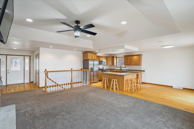 kitchen with a breakfast bar, appliances with stainless steel finishes, a kitchen island, a raised ceiling, and light wood-type flooring