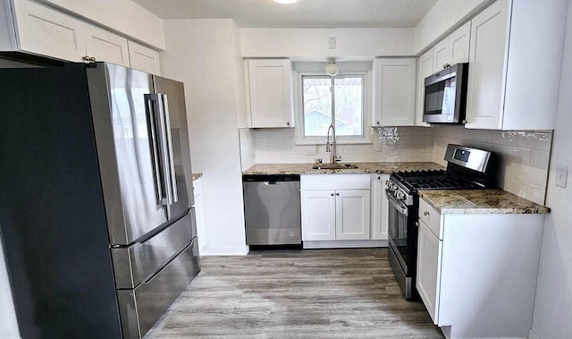 kitchen with tasteful backsplash, white cabinetry, sink, light hardwood / wood-style floors, and stainless steel appliances