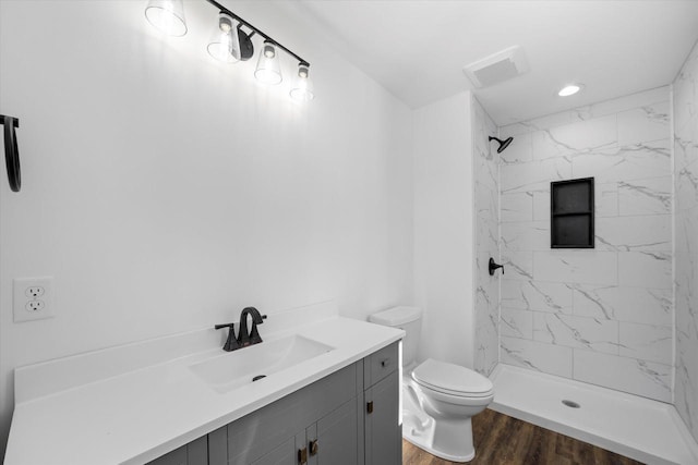 bathroom featuring a tile shower, vanity, hardwood / wood-style floors, and toilet