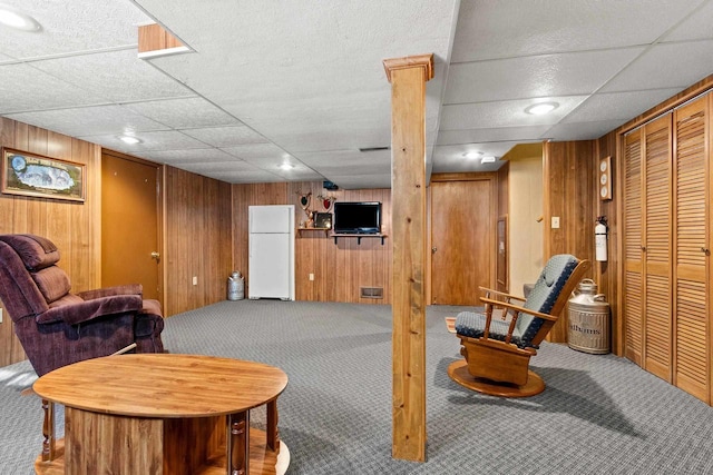 carpeted living room featuring wooden walls and a drop ceiling