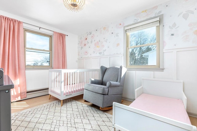 bedroom with a crib, a baseboard radiator, and light wood-type flooring