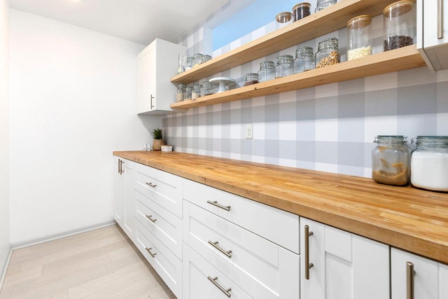 bar with wood counters, light hardwood / wood-style floors, and white cabinets