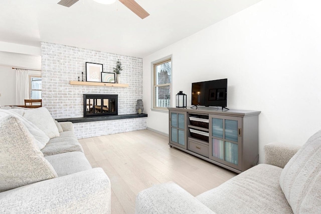 living room with ceiling fan, a brick fireplace, and light hardwood / wood-style floors