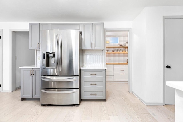 kitchen with light wood-type flooring, gray cabinets, stainless steel fridge with ice dispenser, and backsplash