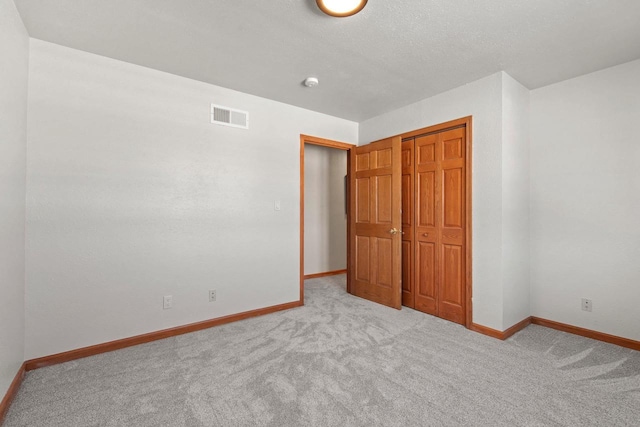 unfurnished bedroom featuring light carpet, a closet, and a textured ceiling