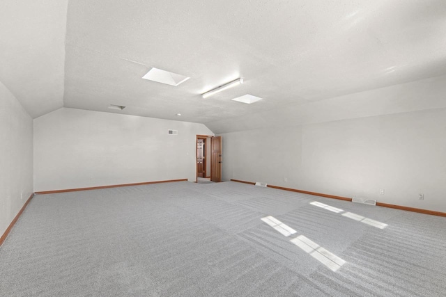 additional living space featuring light carpet, lofted ceiling with skylight, and a textured ceiling