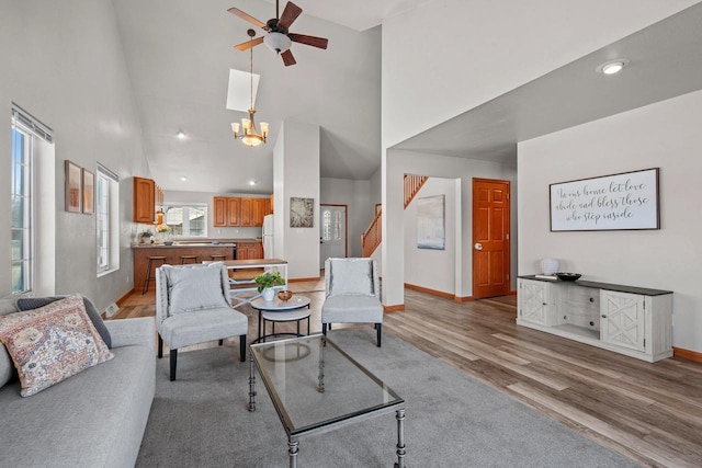 living room with ceiling fan with notable chandelier, high vaulted ceiling, and light hardwood / wood-style flooring