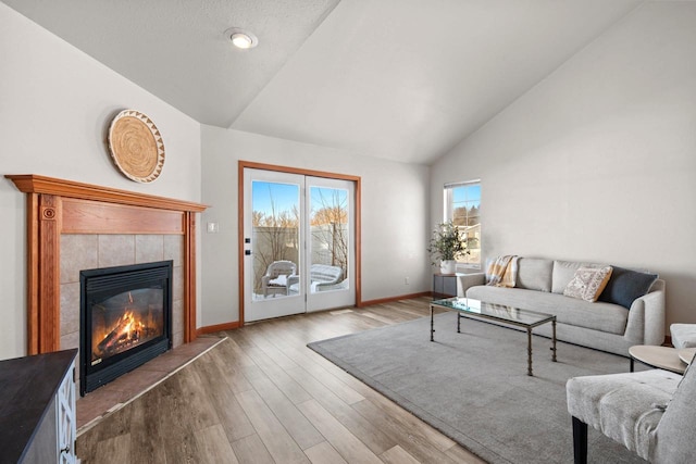 living room featuring high vaulted ceiling, a tile fireplace, and light hardwood / wood-style flooring