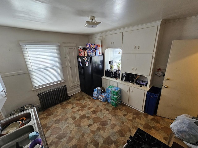 kitchen featuring white cabinetry, radiator heating unit, and black fridge with ice dispenser