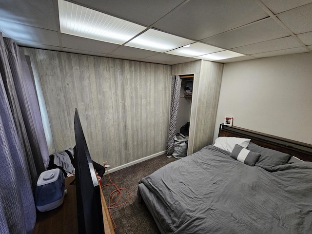 bedroom with a drop ceiling, wooden walls, and dark colored carpet