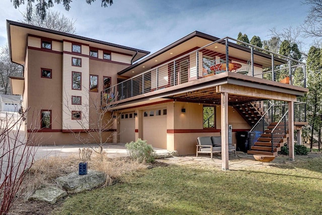 rear view of property featuring a patio, stairway, an attached garage, a yard, and stucco siding