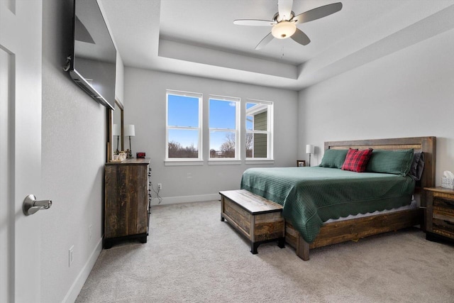 bedroom featuring a raised ceiling, light colored carpet, and ceiling fan