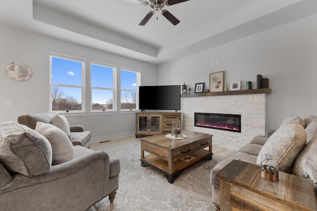 living room with ceiling fan, a tray ceiling, and light hardwood / wood-style floors