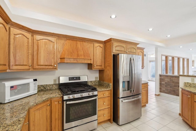 kitchen with custom exhaust hood, appliances with stainless steel finishes, dark stone countertops, and light tile patterned floors