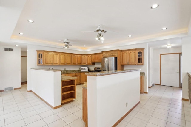 kitchen with light tile patterned flooring, a center island, a raised ceiling, ceiling fan, and stainless steel appliances