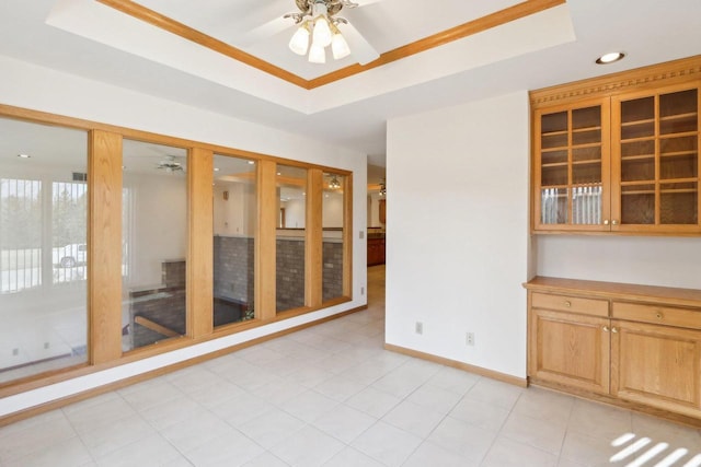 tiled empty room featuring ceiling fan and a tray ceiling