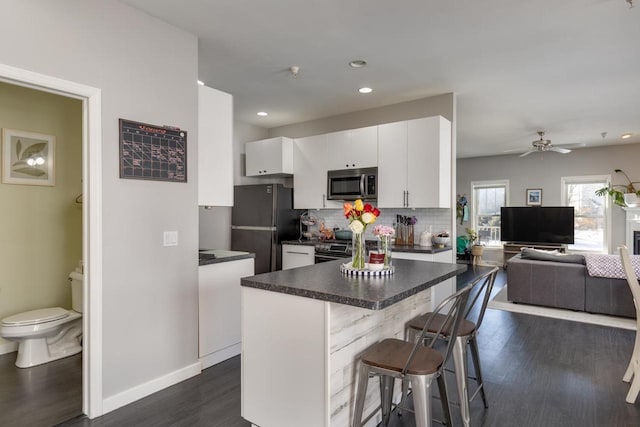 kitchen featuring white cabinets, dark wood-type flooring, a kitchen breakfast bar, and black refrigerator