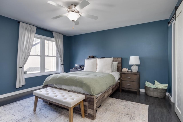 bedroom with dark hardwood / wood-style floors, ceiling fan, and a barn door