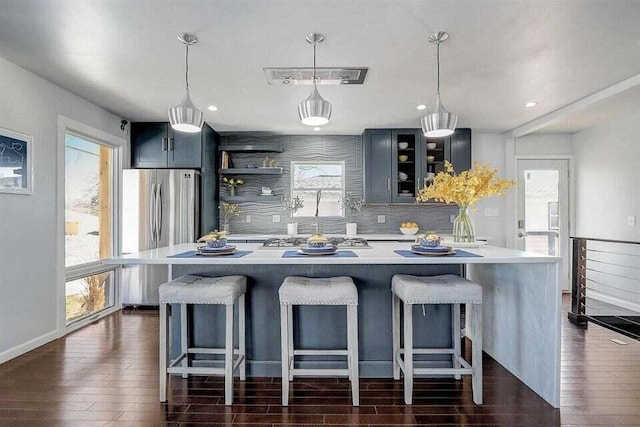 kitchen featuring stainless steel refrigerator, decorative light fixtures, a breakfast bar, and dark wood-type flooring