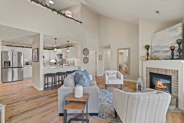 living room with a fireplace, light hardwood / wood-style flooring, high vaulted ceiling, and sink