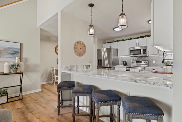 kitchen with a breakfast bar area, appliances with stainless steel finishes, white cabinetry, light stone countertops, and kitchen peninsula