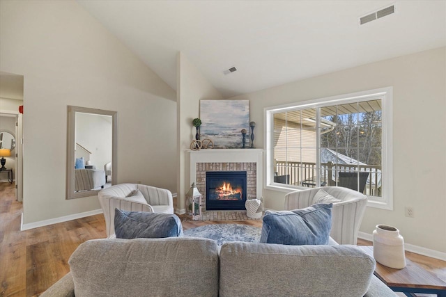 living room with high vaulted ceiling, light hardwood / wood-style floors, and a brick fireplace