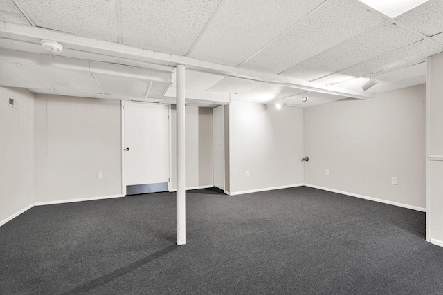 basement featuring a drop ceiling and dark colored carpet