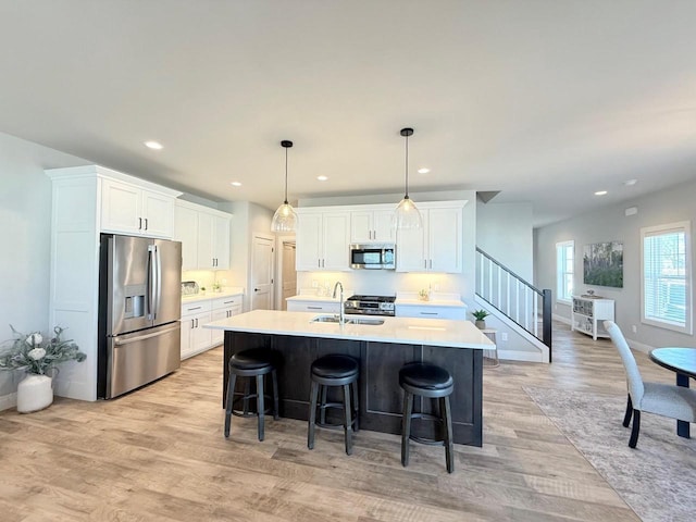 kitchen featuring stainless steel appliances, an island with sink, pendant lighting, and white cabinets