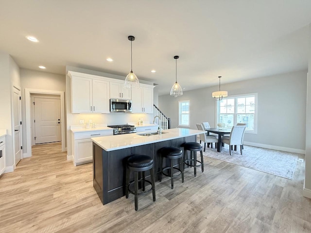 kitchen with pendant lighting, sink, stainless steel appliances, white cabinets, and a center island with sink