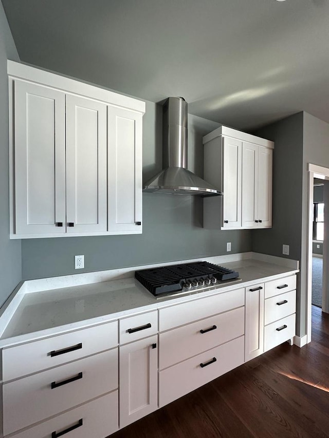 kitchen featuring dark wood-type flooring, wall chimney exhaust hood, stainless steel gas cooktop, and white cabinets