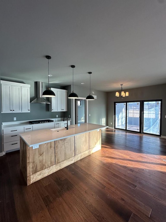 kitchen featuring white cabinets, hanging light fixtures, a large island, black gas stovetop, and wall chimney range hood