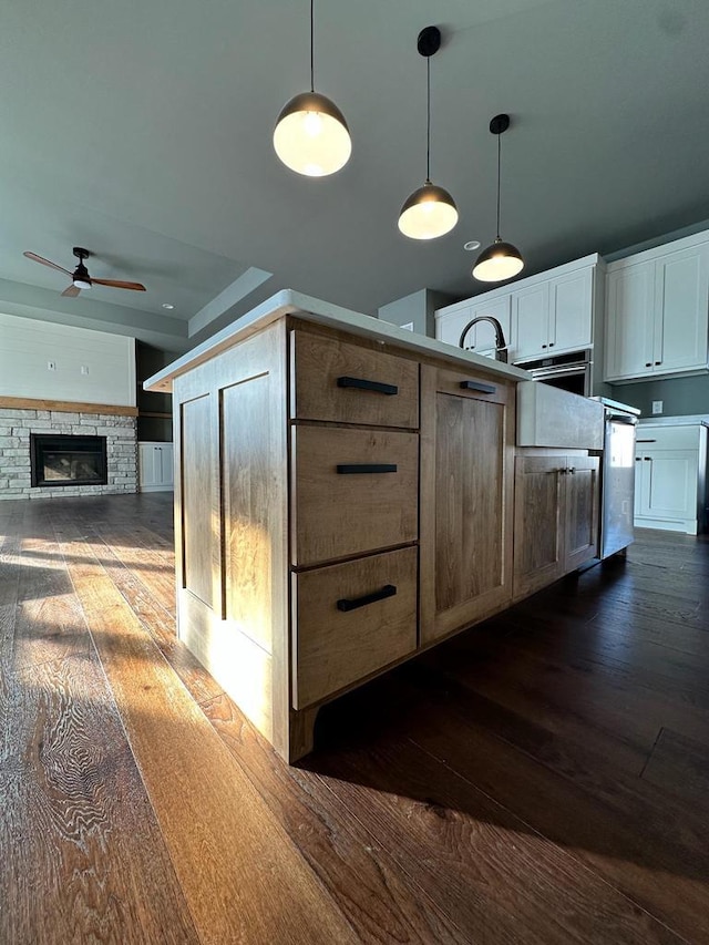 kitchen with dark hardwood / wood-style flooring, pendant lighting, ceiling fan, a fireplace, and white cabinets