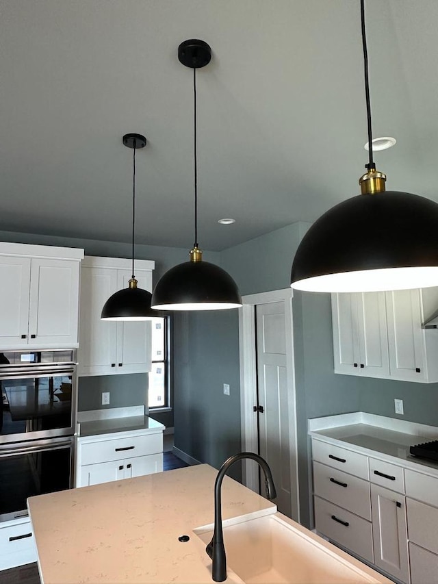 kitchen with stainless steel double oven, white cabinets, light stone counters, and decorative light fixtures