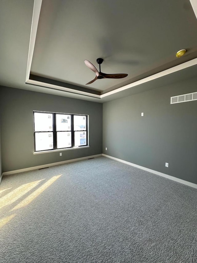 carpeted spare room featuring a raised ceiling and ceiling fan