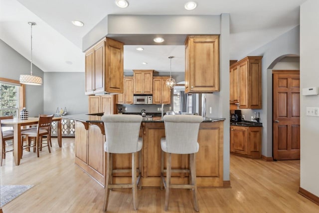 N33W29204 Millridge Rd, Pewaukee, WI 53072 - kitchen featuring light hardwood / wood-style flooring, a kitchen breakfast bar, dark stone counters, decorative light fixtures, and vaulted ceiling