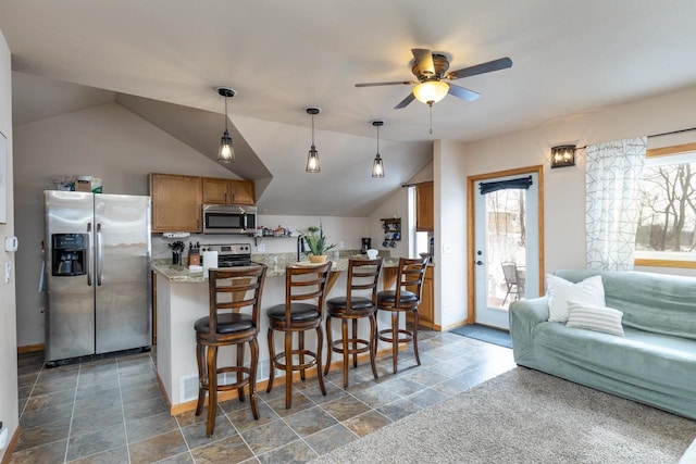 kitchen featuring stainless steel appliances, vaulted ceiling, light stone counters, a breakfast bar area, and pendant lighting