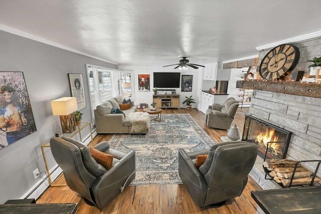 living room with a stone fireplace, baseboard heating, ornamental molding, ceiling fan, and light hardwood / wood-style floors