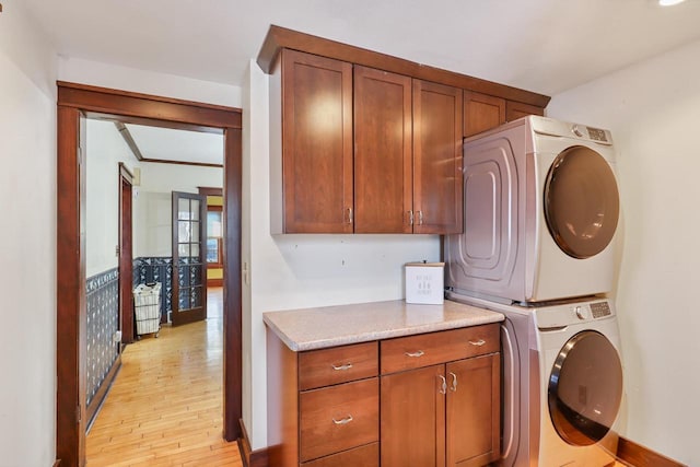 laundry area with stacked washer / drying machine, cabinets, and light wood-type flooring