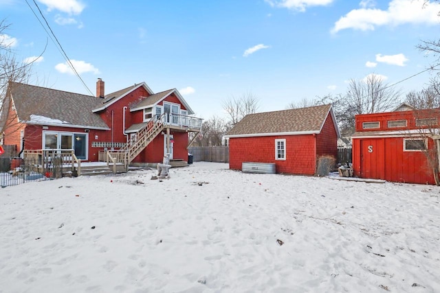 snow covered back of property with a deck and a shed