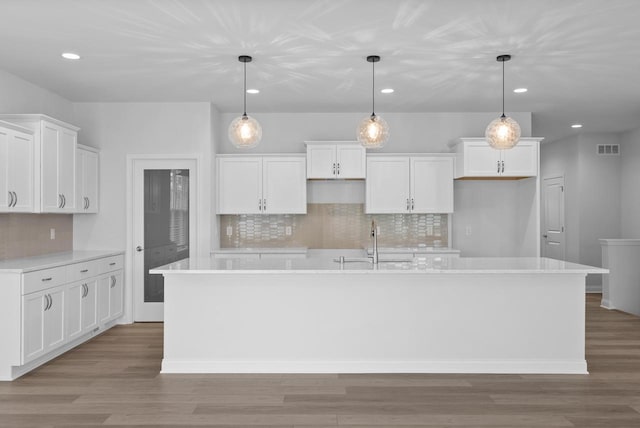 kitchen with a kitchen island with sink, hanging light fixtures, sink, and white cabinets