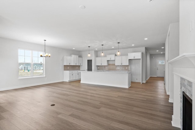 unfurnished living room featuring an inviting chandelier, sink, and light hardwood / wood-style flooring