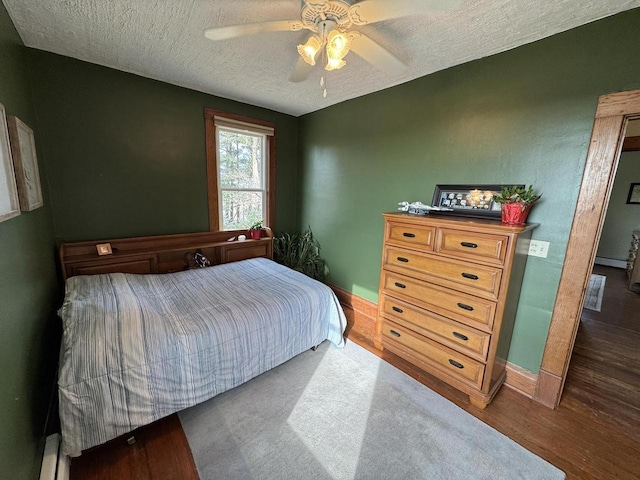 bedroom with ceiling fan, dark hardwood / wood-style floors, a textured ceiling, and a baseboard radiator