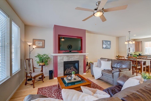 living room with ceiling fan with notable chandelier, light hardwood / wood-style flooring, and a tiled fireplace